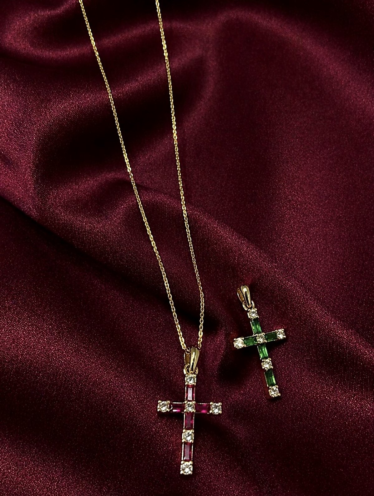 Deux pendentifs croix dorés sertis de pierres rouges, vertes et claires sur satin bordeaux